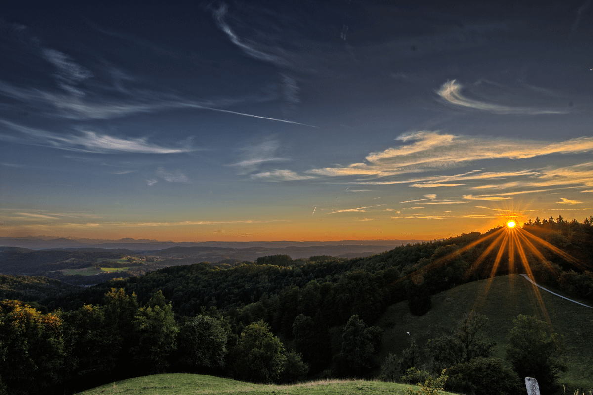 Uma paisagem serena ao nascer do sol, com raios de luz filtrando-se por entre nuvens, simbolizando esperança e a presença divina.