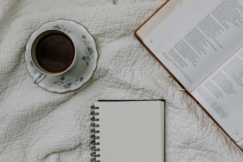 Mesa com uma Bíblia aberta, um caderno de anotações, uma caneta e uma xícara de café, representando um momento de devocional e estudo pessoal.