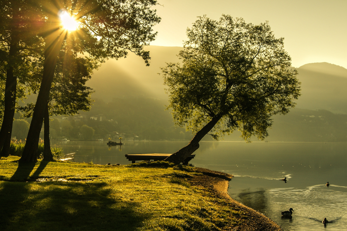 Uma paisagem serena ao amanhecer, com raios de sol rompendo as nuvens, simbolizando um novo começo e perdão.
